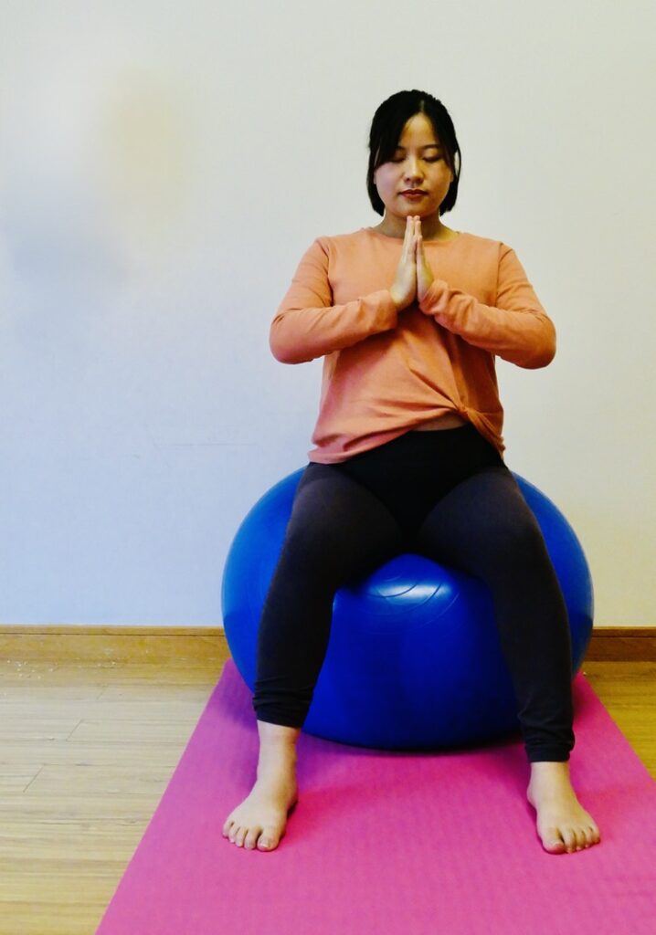 A pregnant lady sitting on exercise ball practicing yoga